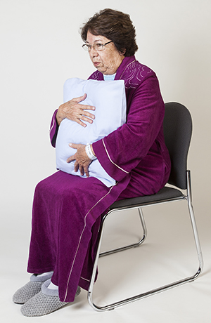 Woman sitting and holding pillow to chest.