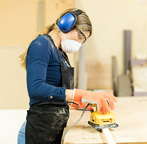 Woman wearing a mask and goggles, holding a power sander.