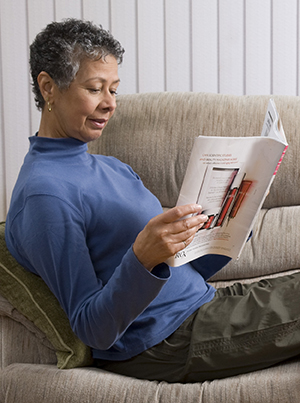 Mujer leyendo una revista en un sofá con los pies levantados.
