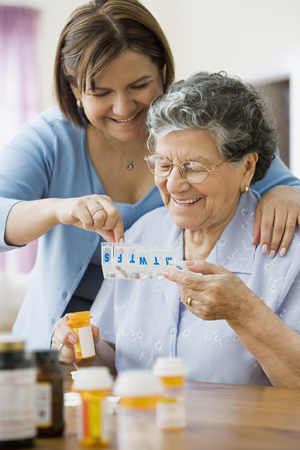 Mujer que ayuda a una mujer mayor con un organizador de medicamentos.
