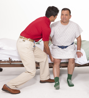 Fisioterapeuta que ayuda a un hombre a levantarse de una cama de hospital.
