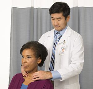 Médico que palpa el cuello de una mujer para examinar su glándula tiroidea.