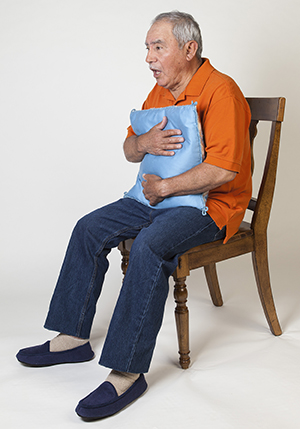 Hombre que sostiene una almohada contra su pecho y tose.