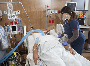 Proveedor de atención médica atendiendo a un paciente intubado en la unidad de cuidados intensivos.