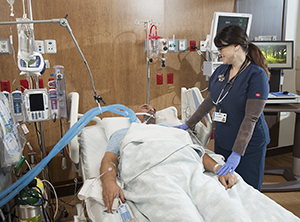 Proveedor de atención médica atendiendo a un hombre intubado en una cama de la unidad de cuidados intensivos.