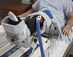 Hombre acostada en una cama de hospital con una rodilla sostenida por un equipo de movimiento pasivo continuo.