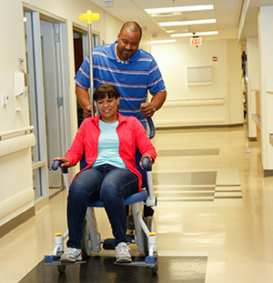 Hombre que empuja una silla de ruedas con una mujer por el corredor del hospital.